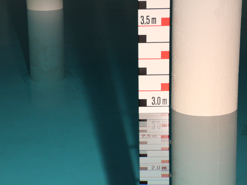 Klares Wasser in einem Becken, darin befinden sich Säulen und ein Messstab