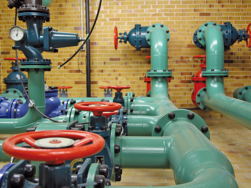 Massive Wasserleitungen in einem Gebäude in pastellgrüner Farbe.